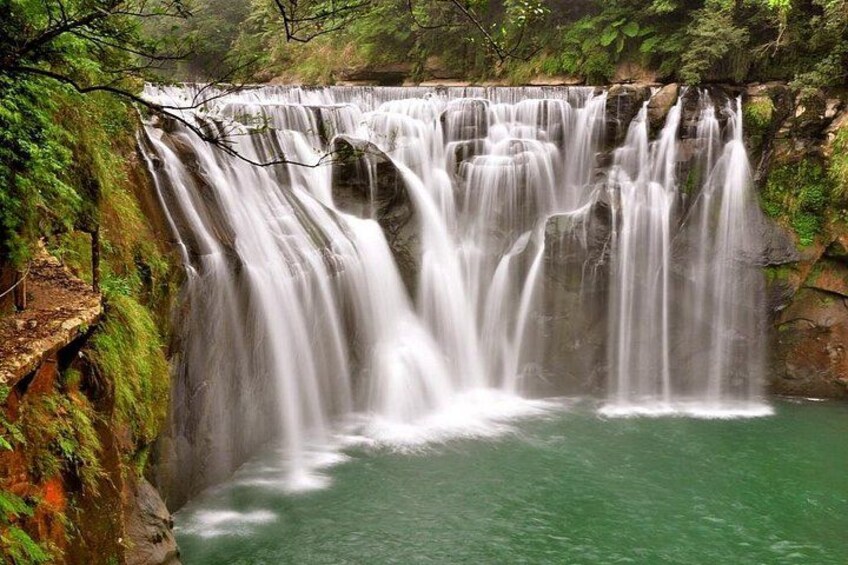A multi-tiered waterfall cascading into a pool surrounded by lush greenery. 2