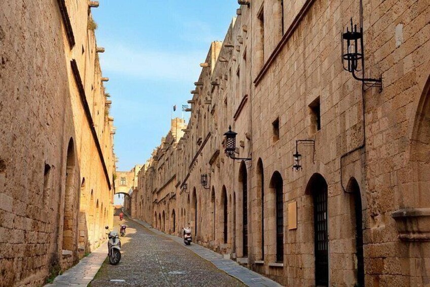 A narrow cobblestone street flanked by historic stone buildings with arched windows and doorways. 4