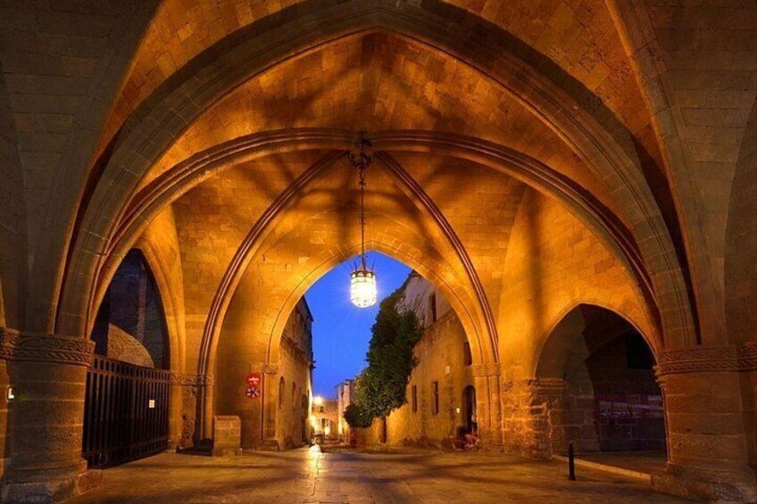 An illuminated stone archway with a hanging light fixture, leading to a tree-lined street at dusk. 3