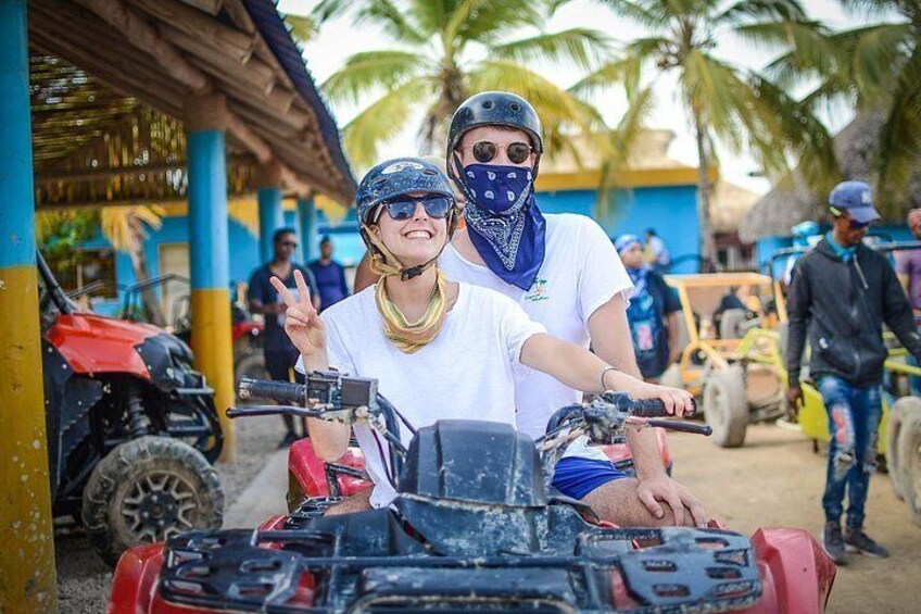 Two people on a quad bike, a red vehicle, and a yellow vehicle in a tropical setting with palm trees. 2