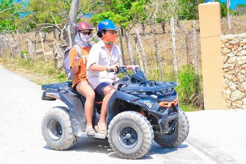 Twee personen op een quad op een verharde weg, met een stenen muur en een wijngaard op de achtergrond. 3