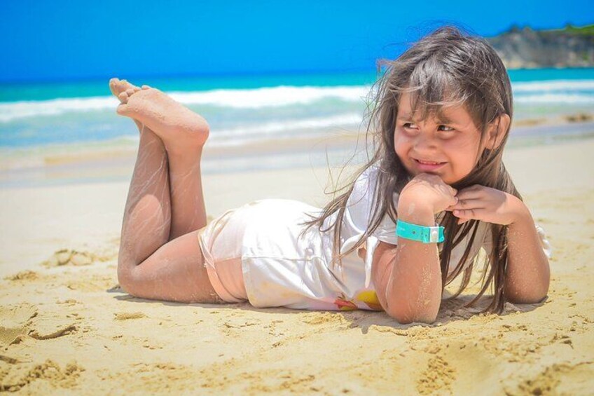 Un niño recostado en una playa arenosa con un cielo azul despejado y el océano al fondo. 4