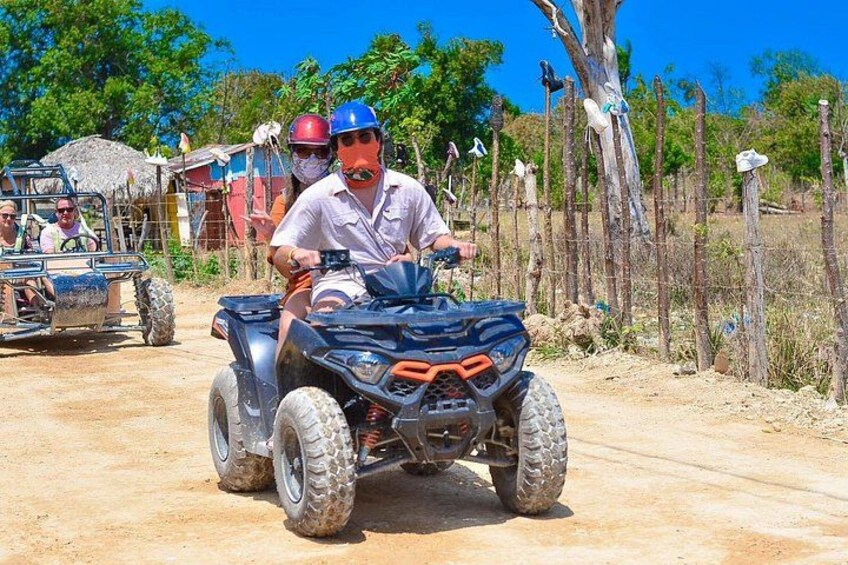 A person riding an ATV on a dirt road with a fence and trees in the background. 2