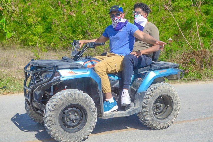 Een blauwe quad met brede offroadbanden, twee inzittenden in vrijetijdskleding, en een groene natuur achtergrond. 5
