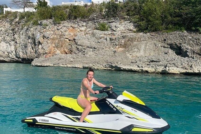 A person on a Yamaha jet ski in clear water with rocky terrain and vegetation in the background. 2
