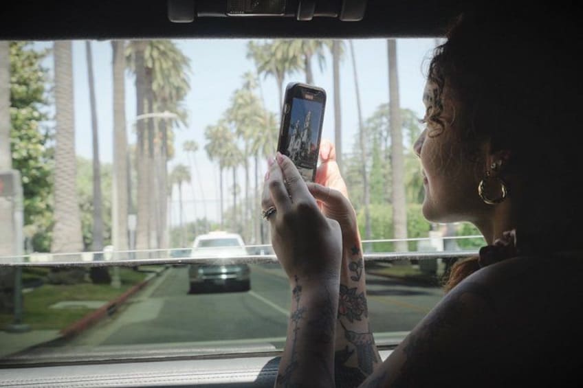 Una persona sosteniendo un teléfono inteligente, mirando por la ventana de un coche con palmeras al fondo. 4