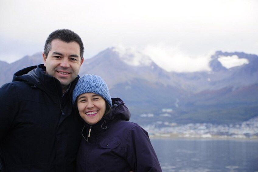 A person in a blue jacket and a child in a blue hat standing in front of a mountainous landscape with a body of water in the background. 2
