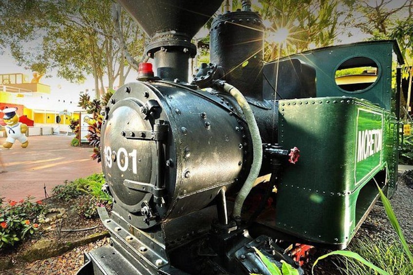 A vintage steam locomotive with the number 1901, parked outdoors with greenery and a building in the background. 5