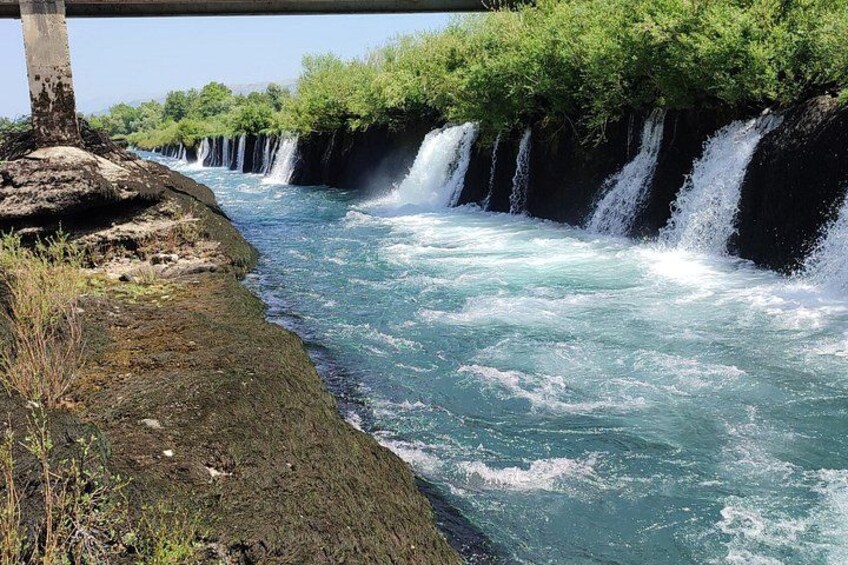 A river with multiple waterfalls, a rocky bank, and lush greenery. 4
