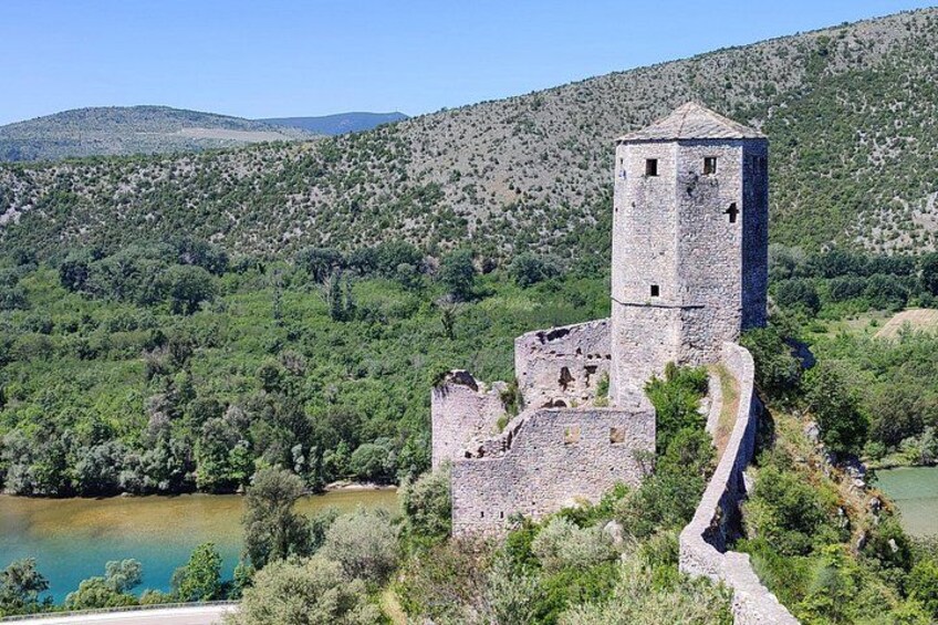 A stone tower and ruins on a hillside overlooking a body of water. 3