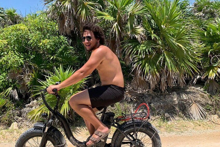 A person riding a bicycle with a basket, surrounded by palm trees and greenery. 1