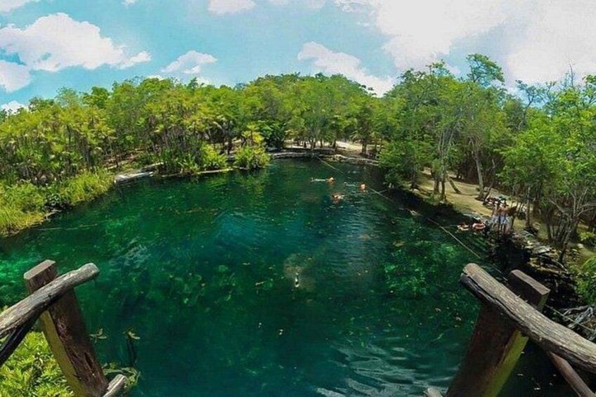 A clear water body surrounded by dense greenery, wooden walkways, and a few people in the distance. 5