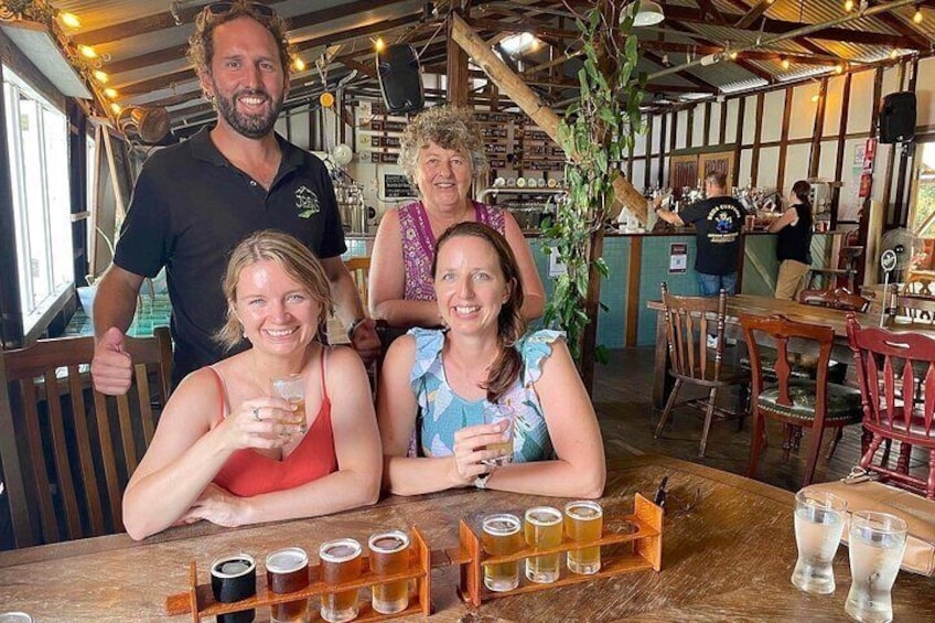 A group of people sitting at a wooden table with drinks in shot glasses. 1