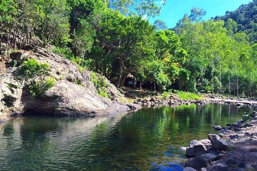A calm river with rocks, dense green trees, and a small house on a hill. 1