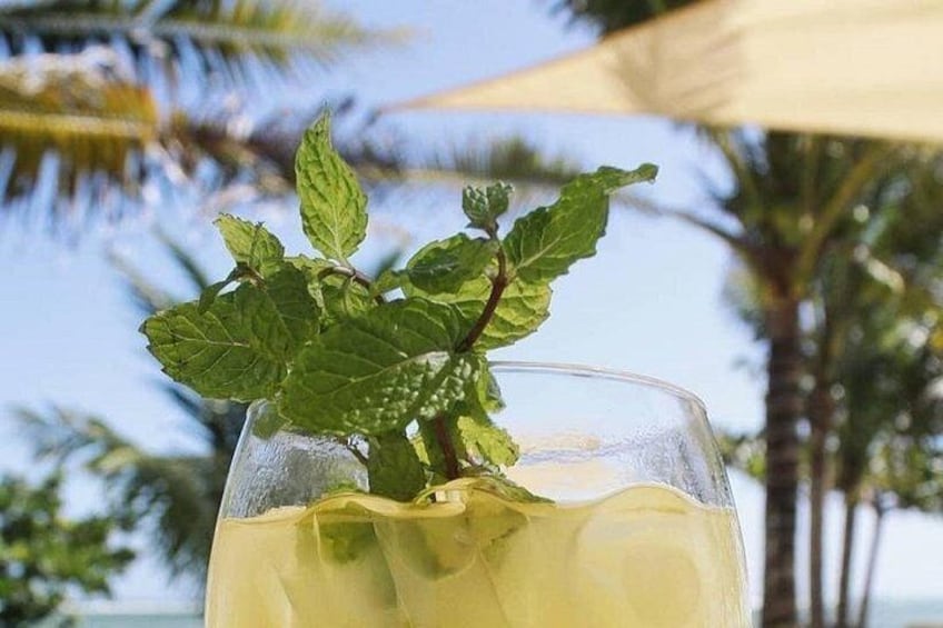 Een glas met een verfrissend drankje en muntblaadjes, buiten met palmbomen op de achtergrond. 2