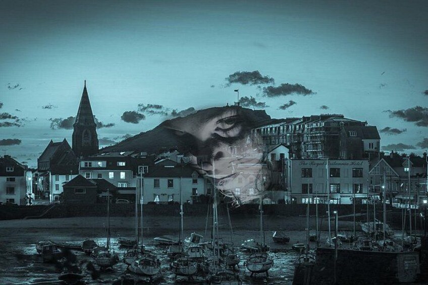 A coastal town with a prominent church steeple, a large building with signage, and boats in the water. 1