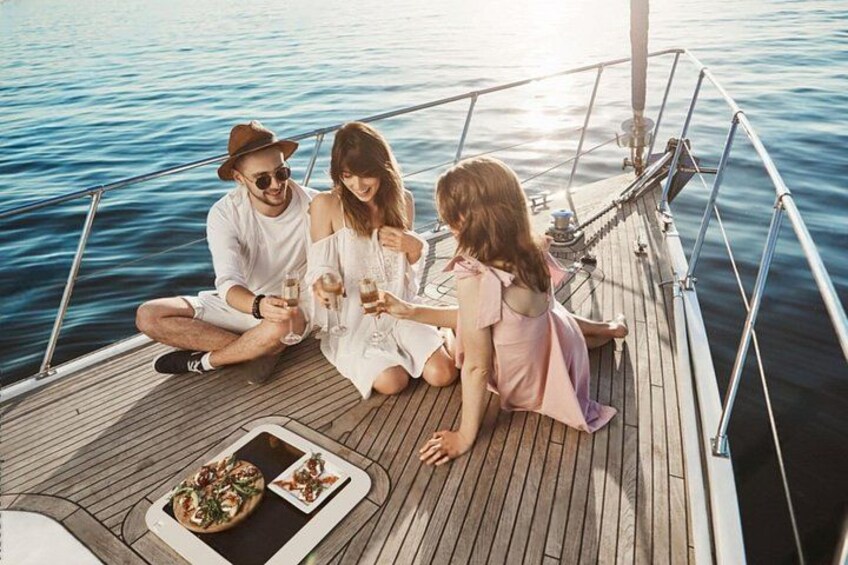 A boat with people sitting on the deck, holding drinks, and a plate of food. 2