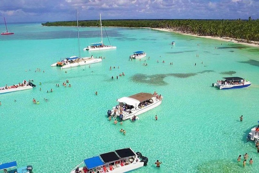 Una playa tropical con agua turquesa cristalina, varios barcos y gente nadando y disfrutando de la playa. 3