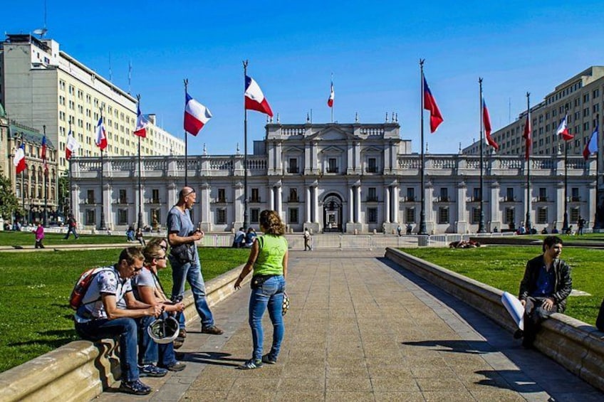 A large building with columns, flags, and people in a courtyard. 1