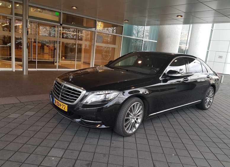 Un sedán negro Mercedes-Benz Clase S estacionado frente a un edificio moderno con grandes ventanales. 1