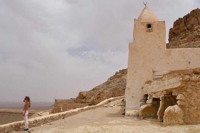 A desert landscape with a small, isolated building with a conical roof, situated on a rocky outcrop. 2