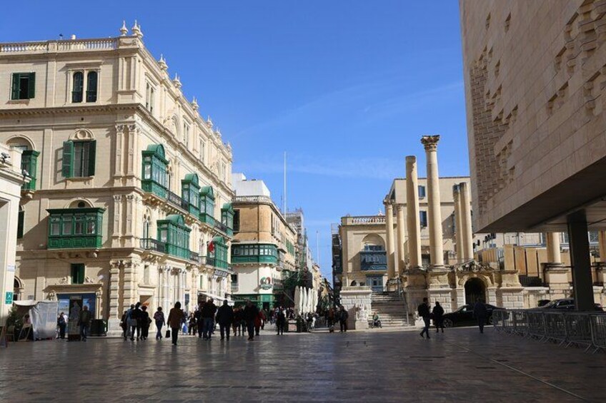 A historic square with classical architecture, a fountain, and a clear blue sky. 1