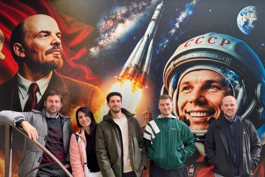 Un grupo de personas con un cohete y un casco espacial al fondo. 2