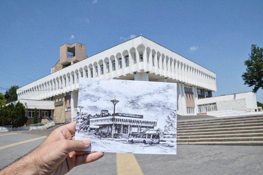 A hand holding a black and white photo of a building with a large arched entrance and a clock tower. 3