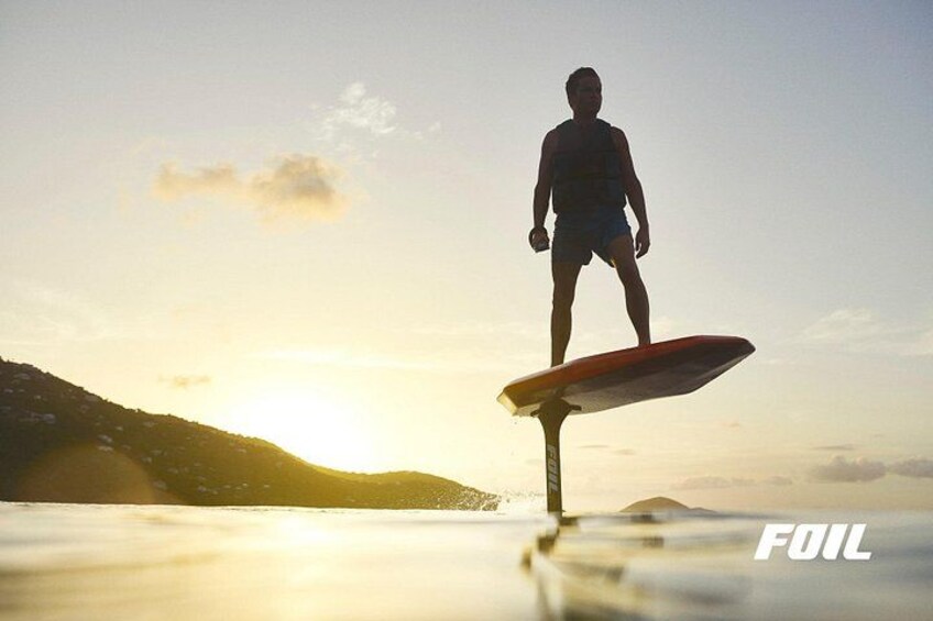 A person standing on a surfboard with a sunset in the background. 2