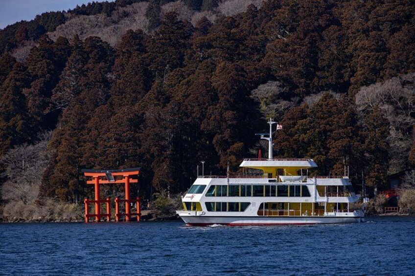 A riverboat with a white and yellow exterior, a red torii gate, and a forested hill in the background. 2