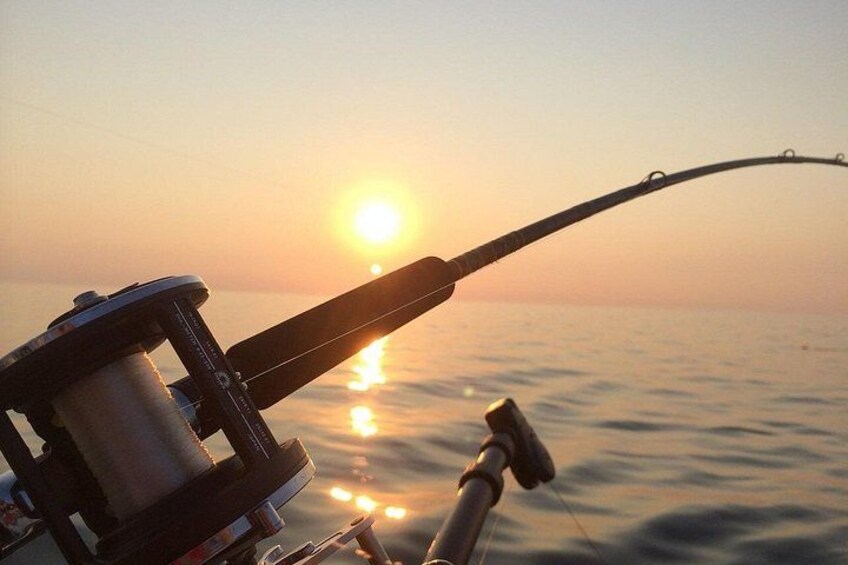 Une canne à pêche avec un moulinet, et un coucher de soleil sur l’océan. 5