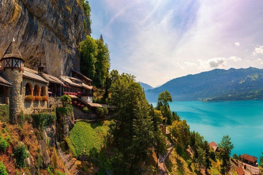 A mountain lodge with a lake view, surrounded by lush greenery and rocky cliffs. 4