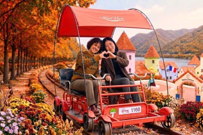 A red carriage with a canopy, a person making a heart shape with their hands, and a scenic view of a village with colorful buildings and a lake. 1