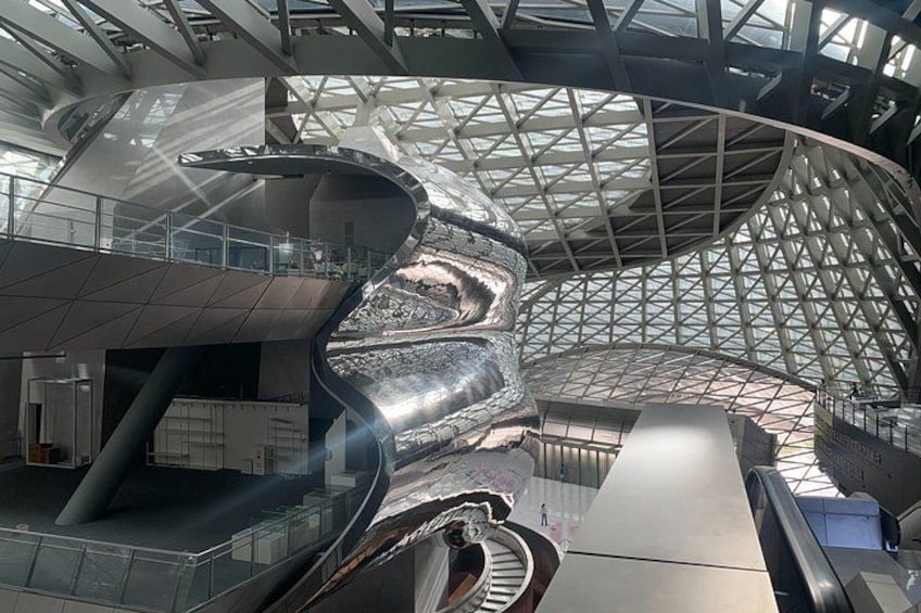 A modern architectural structure with a curved metallic sculpture and a glass roof. 1
