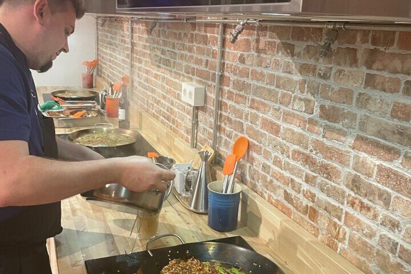 Une personne cuisine dans une cuisine aux murs en briques, équipée d’une cuisinière et de divers ustensiles de cuisine. 4