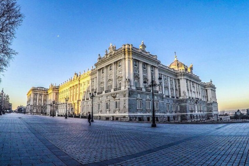 Un grande edificio storico dall'architettura classica, con una piazza lastricata di fronte e un cielo sereno. 3