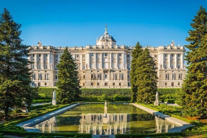 Un grande edificio classico con una facciata simmetrica, una cupola centrale e un giardino formale con una vasca specchiante. 2