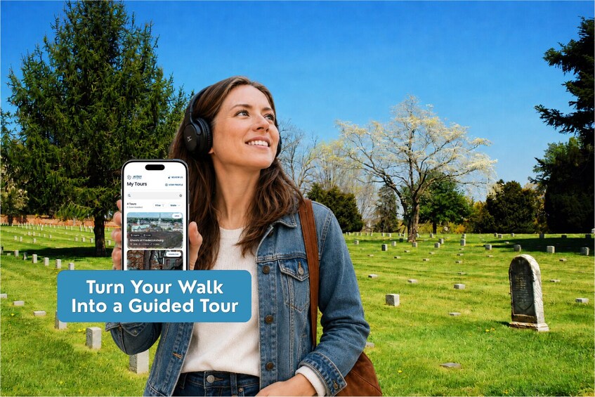 A person holding a smartphone with a travel app interface, standing in a cemetery with headstones and trees in the background. 3