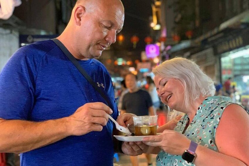 A man and a woman eating at a street food stall in an urban setting. 2