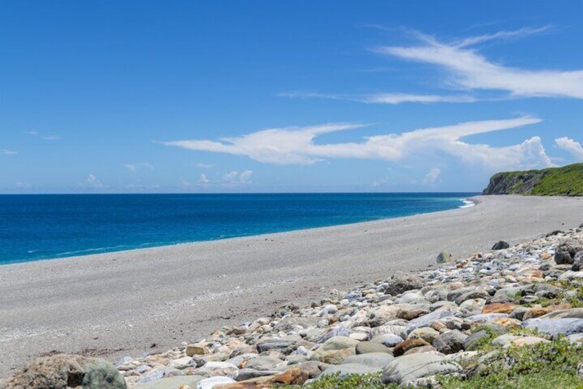 A beach with clear blue water, a rocky shoreline, and a grassy cliff. 4
