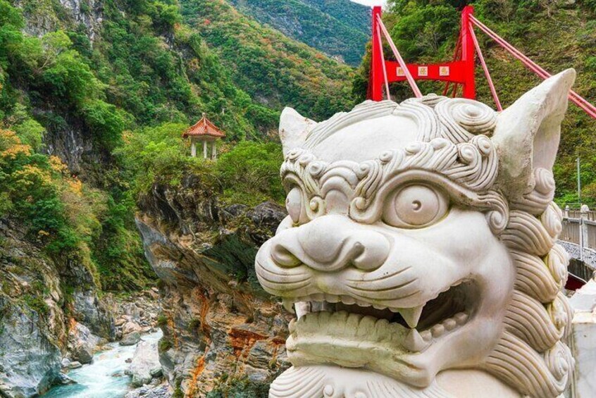 A stone lion statue with a river and a red bridge in the background. 1
