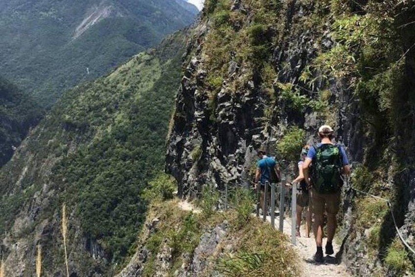 Hikers on a mountain trail surrounded by steep cliffs and dense greenery. 3
