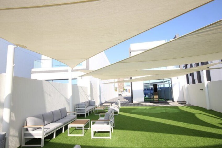 An outdoor lounge area with white furniture, green artificial turf, and a large canopy. 1