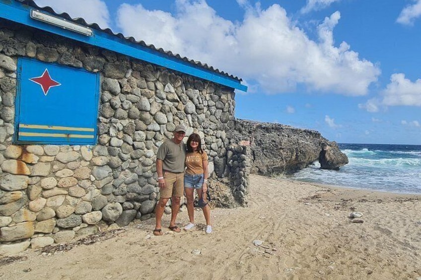 A stone building with a blue roof and a flag, a sandy beach, and the ocean. 3