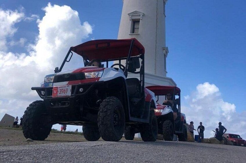 A large off-road vehicle parked in front of a white tower. 4