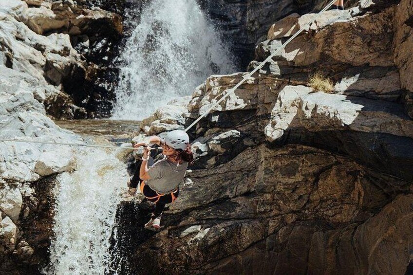 Una persona descendiendo en rappel por un risco cerca de una cascada. 2
