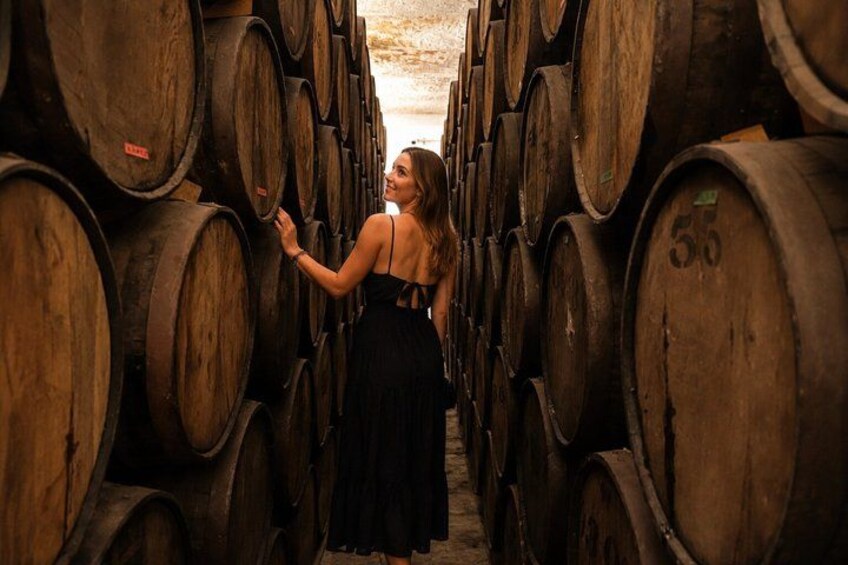Une femme vêtue d’une robe noire se tient entre des rangées de barriques de vin en bois. 4