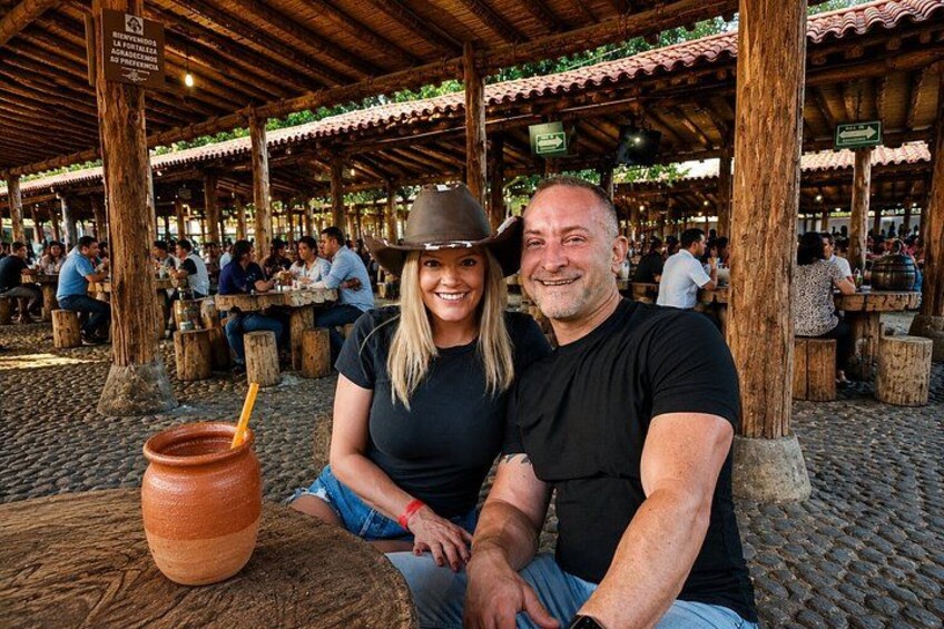 A couple sitting at a wooden table with a large clay pot. 3