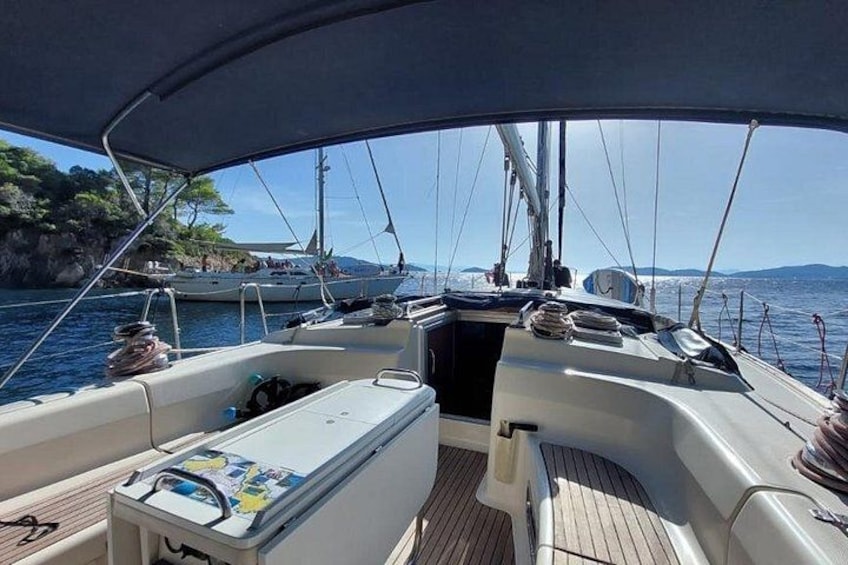 A sailboat deck with a cooler, a cushioned seating area, and a view of the sea and distant land. 1