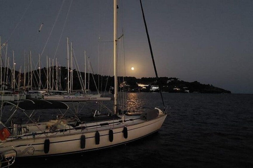 A sailboat docked at a marina with a moonlit background and distant buildings. 2